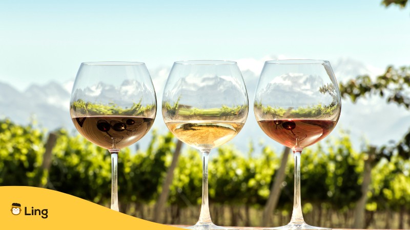 3 Glaeser mit Wein in unterschiedlichen Farben im Hintergrund sind Weinberge