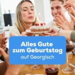 Blonde Frau bläst Kerzen auf Geburtstagstorte während ihre Freunde Alles Gute zum Geburtstag auf Georgisch wünschen