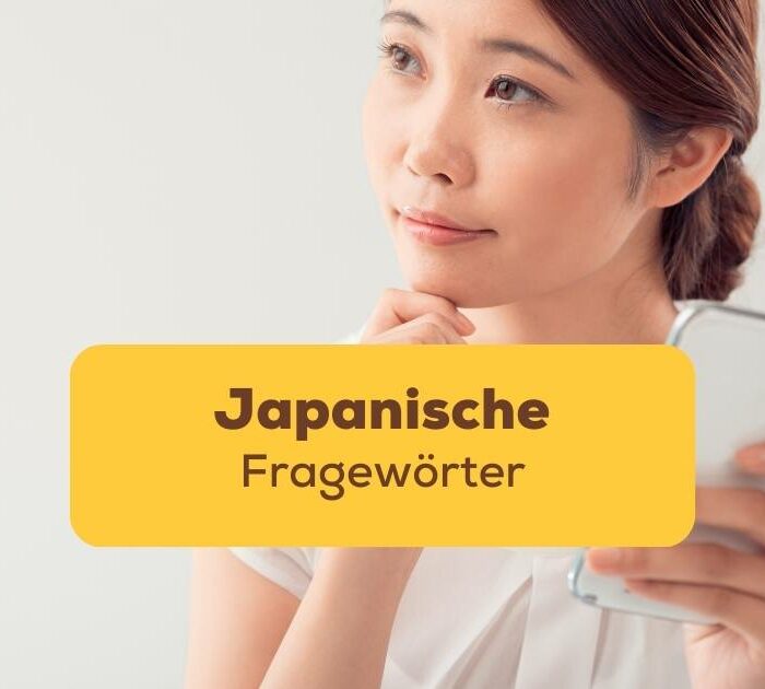 Asiatische Frau sitzt an einem Schreibtisch und hält mit einer Hand einen Notizblock und lernt japanische Fragewörter
