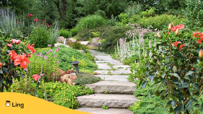 Schön angelegter grüner Garten mit Blumen und einem Steinweg durch, der das bosnische Sprichwort darstellt, das man seinen eigenen Garten reinigen sollte, bevor man anderen sagt, das sie ihre Gärten reinigen sollten