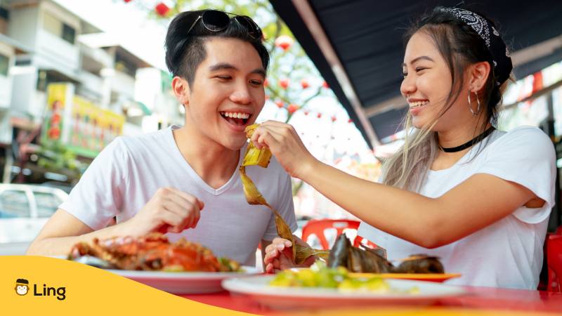 Frau füttert Mann mit leckerem Street food in Kuala Lumpur beim Reisen in Malaysia