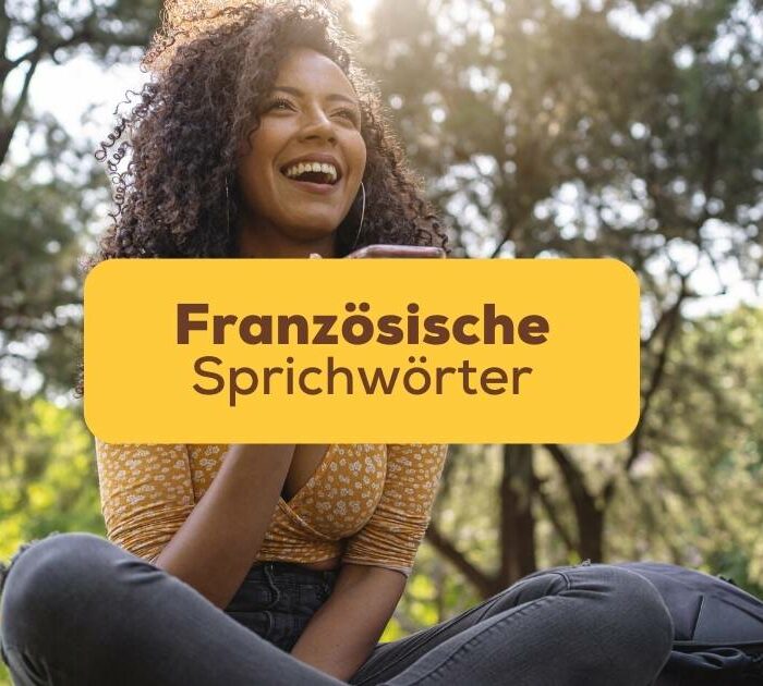 Frau sitzt im Park im Gras und lacht über witzige französische Sprichwörter die sie bei Ling gelesen hat