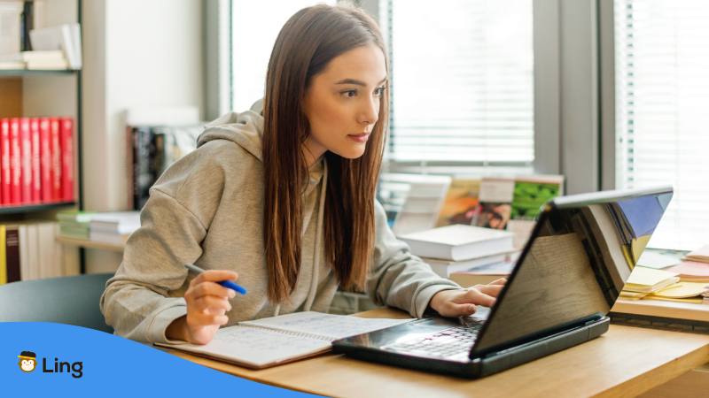 Frau sitzt am Tisch mit einem Laptop und einem Notizblock und lernt Serbisch mit Ling-App