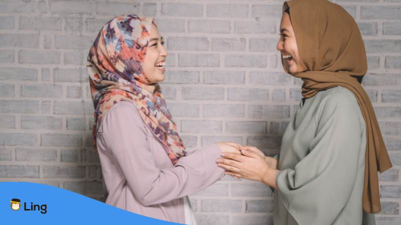 Zwei malaysische Frauen freuen sich zu treffen und schütteln sich respektvoll die Hände um Hallo auf Malaysisch zu sagen