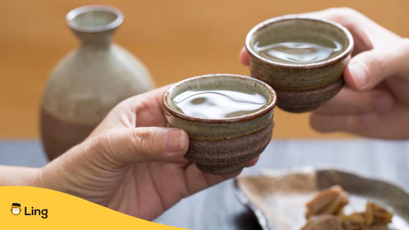 Zwei Hände, die mit einer Tasse Sake jubeln, zeigen das japanische Sprichwort, dass Sake wahre Gefühle zeigt.