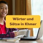 Junger Mann sitzt lächelnd am Schreibtisch und lernt Wörter und Sätze in Khmer mit der Ling-App