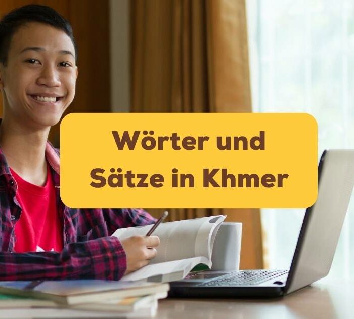 Junger Mann sitzt lächelnd am Schreibtisch und lernt Wörter und Sätze in Khmer mit der Ling-App