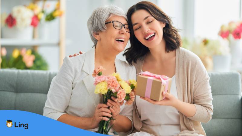 Erwachsene Tochter hält ihre Mutter im Arm und übergibt ihr ein Geschenk und macht ihr Komplimente über ihre Persönlichkeit
