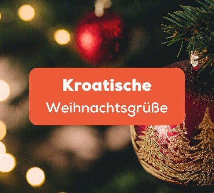 Rote Weihnachtskugeln mit Glitzerdekoration, die an einem grünen Tannenzweig hängen, Kroatische Weihnachtsgrüße