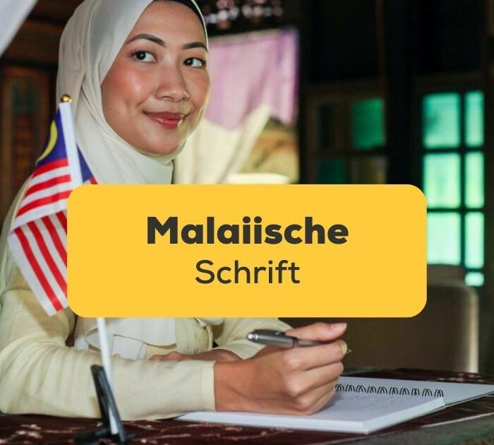 Frau in Malaysia sitzt an einem Schreibtisch mit einer malaysischen Flagge und schreibt die malaiische Schrift