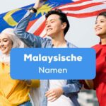Zwei Frauen und ein Mann halten gemeinsam die Flagge von Malaysia über ihren Köpfen, alle drei tragen malaysische Namen