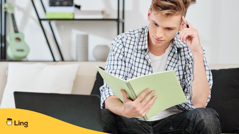 Junger Mann sitzt auf einem Sofa und schaut in seinen Notizblock und versucht mit der Mnemonic Technik eine neue Sprache zu lernen