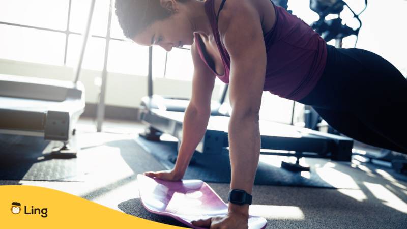 Junge Frau trainiert ihren Oberkörper im Fitnessstudio mit Planks und lernt dabei Bulgarisch