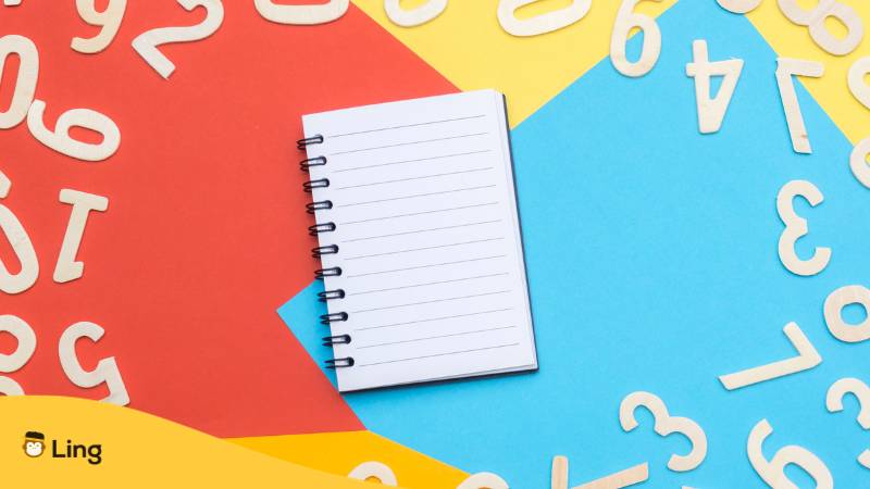 Notizbuch mit linierten Seiten liegt auf buntem Papier, drumherum liegen weiße armenische Zahlen