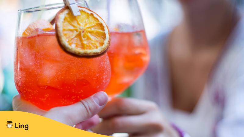 Gläser mit Aperol Spritz stoßen an und sagen Prost auf Italienisch