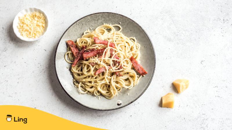 Teller, auf dem Spaghetti Carbonara serviert ist und Schälchen mit Parmesan. Ein köstliches italienisches Essen aus Italien.