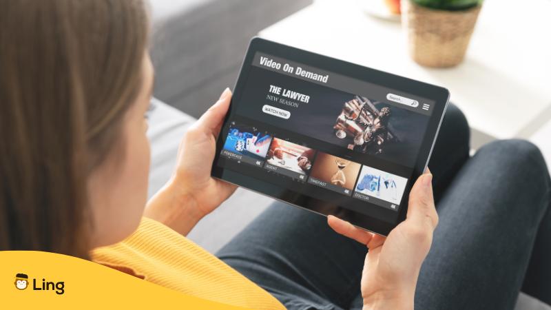 Frau hält ein Tablet in der Hand und schaut einen Film in einer Fremdsprache um ihre Kenntnisse zu verbessern